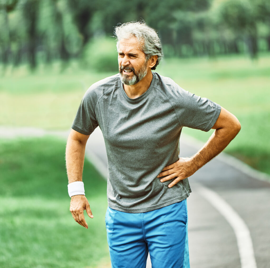 portrait of a senior man exercising and running outdoors having hip or back pain or injury