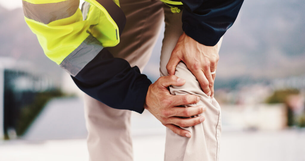 Person, architect and hands with knee pain for injury, construction accident or emergency in city. Closeup, civil engineer or contractor with joint inflammation, sore leg or sprain for arthritis.