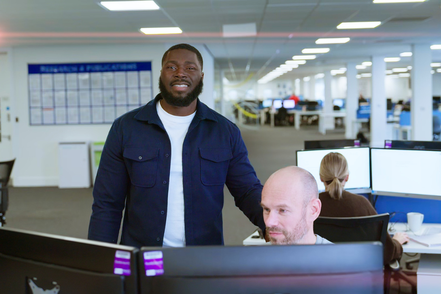 A man and his colleague stand at a desk together smiling at camera