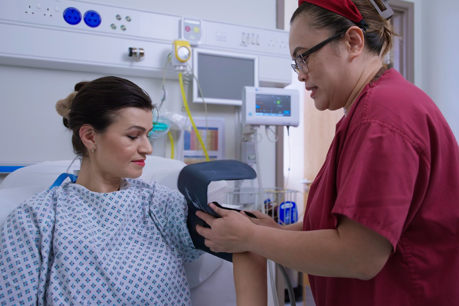 A nurse looks after a patient, about to take her blood pressure with an arm cuff