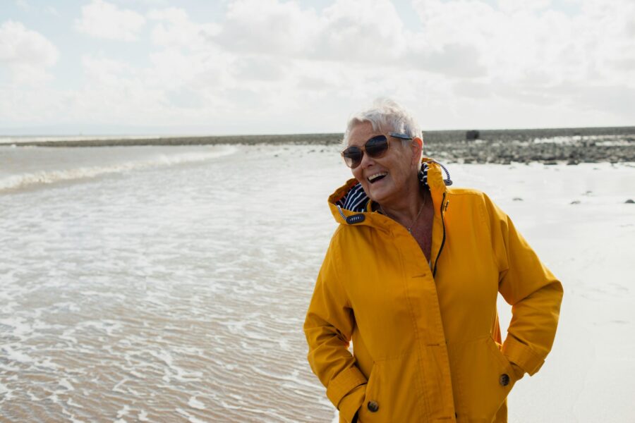 Smiling lady on beach wearing yellow jacket.